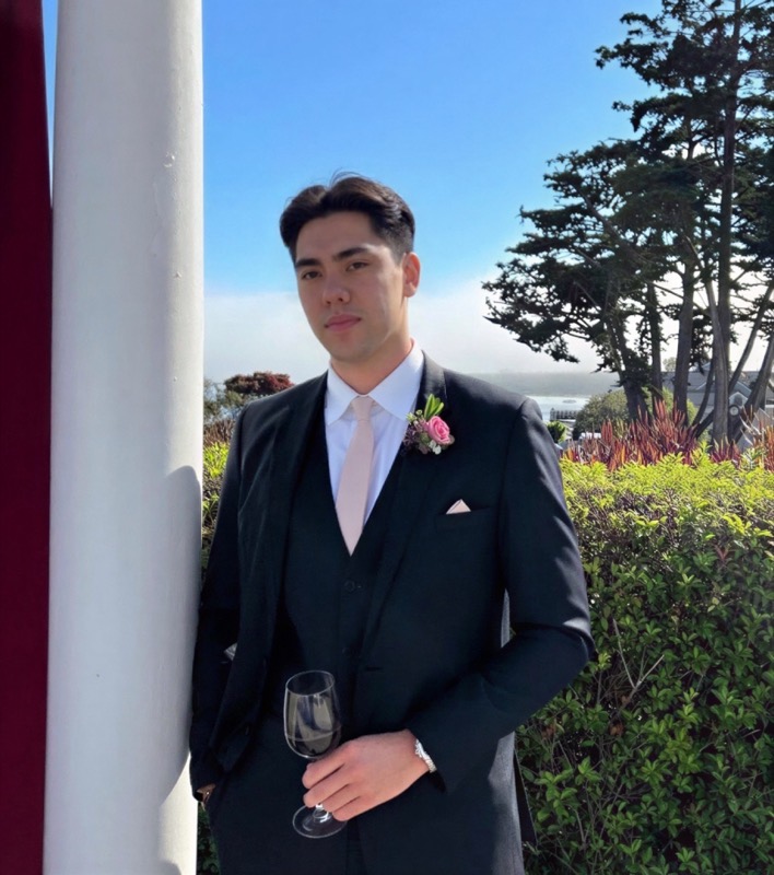 Matthew Stevens in a navy three-piece suit with a boutonniere, holding a wine glass in a garden