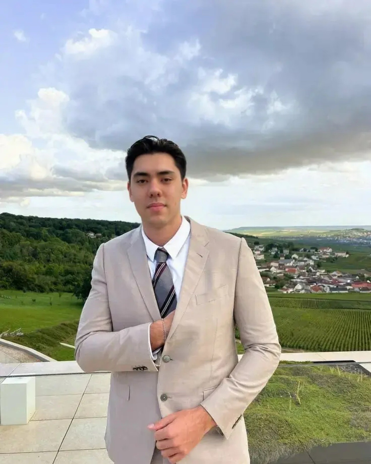 Matthew Stevens in a beige suit and striped tie on a terrace above a green valley