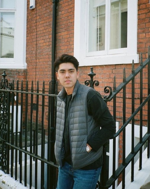 Matthew Stevens in a grey puffer vest beside a red-brick London townhouse