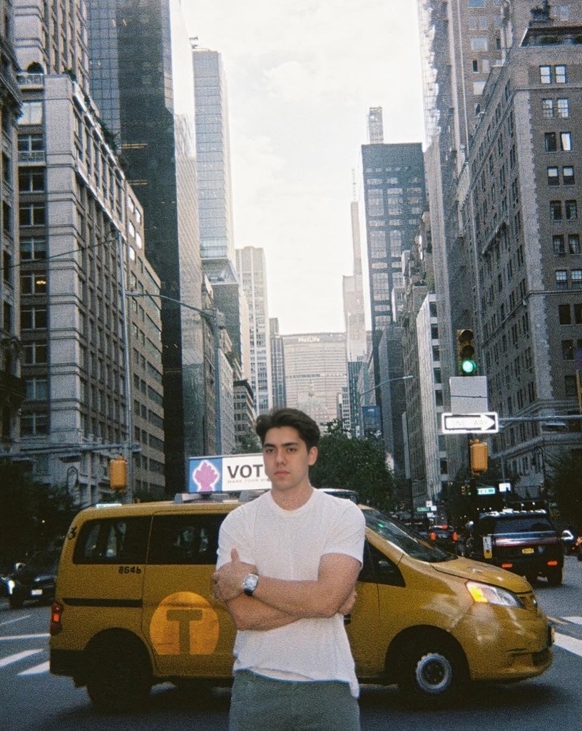 Matthew Stevens in a white T-shirt with arms crossed on a New York avenue, a yellow cab behind