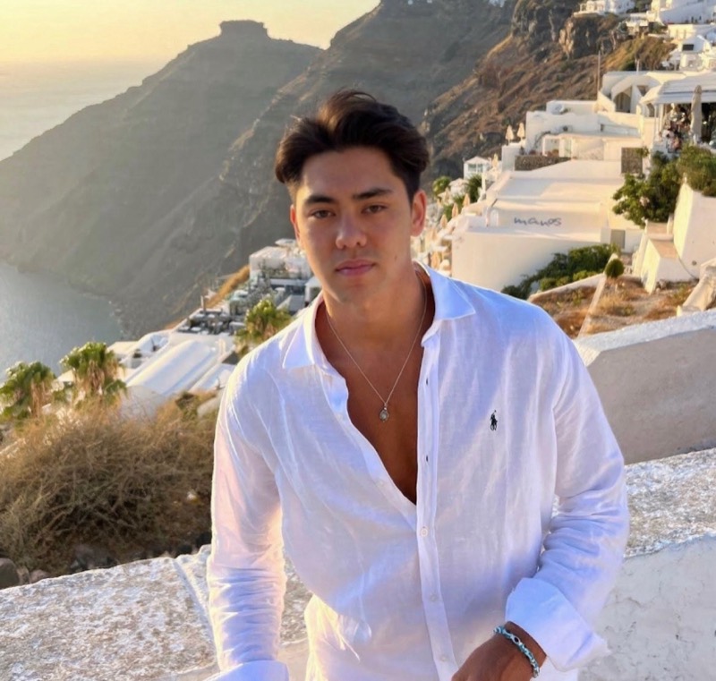 Matthew Stevens in a white open-collar shirt above the Santorini cliffs at golden hour
